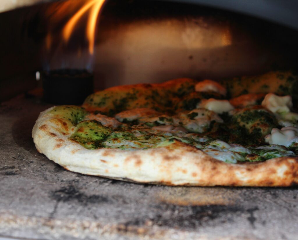 פיצה עם פסטו וגבינה נאפית בתנור עם להבה בוערת.